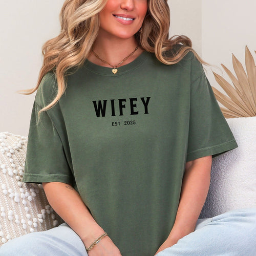 Hemp color T-shirt with the text "WIFEY EST 2025" in bold black lettering, celebrating a newlywed or engaged status. The modern minimalist design makes it perfect for brides, honeymoon outfits, or casual newlywed style.  Ideal for wedding gifts, bridal showers, or anniversary celebrations.