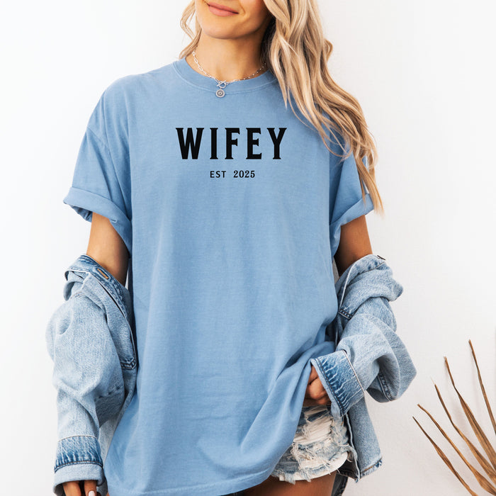 Washed Denim T-shirt with the text "WIFEY EST 2025" in bold black lettering, celebrating a newlywed or engaged status. The modern minimalist design makes it perfect for brides, honeymoon outfits, or casual newlywed style.  Ideal for wedding gifts, bridal showers, or anniversary celebrations.