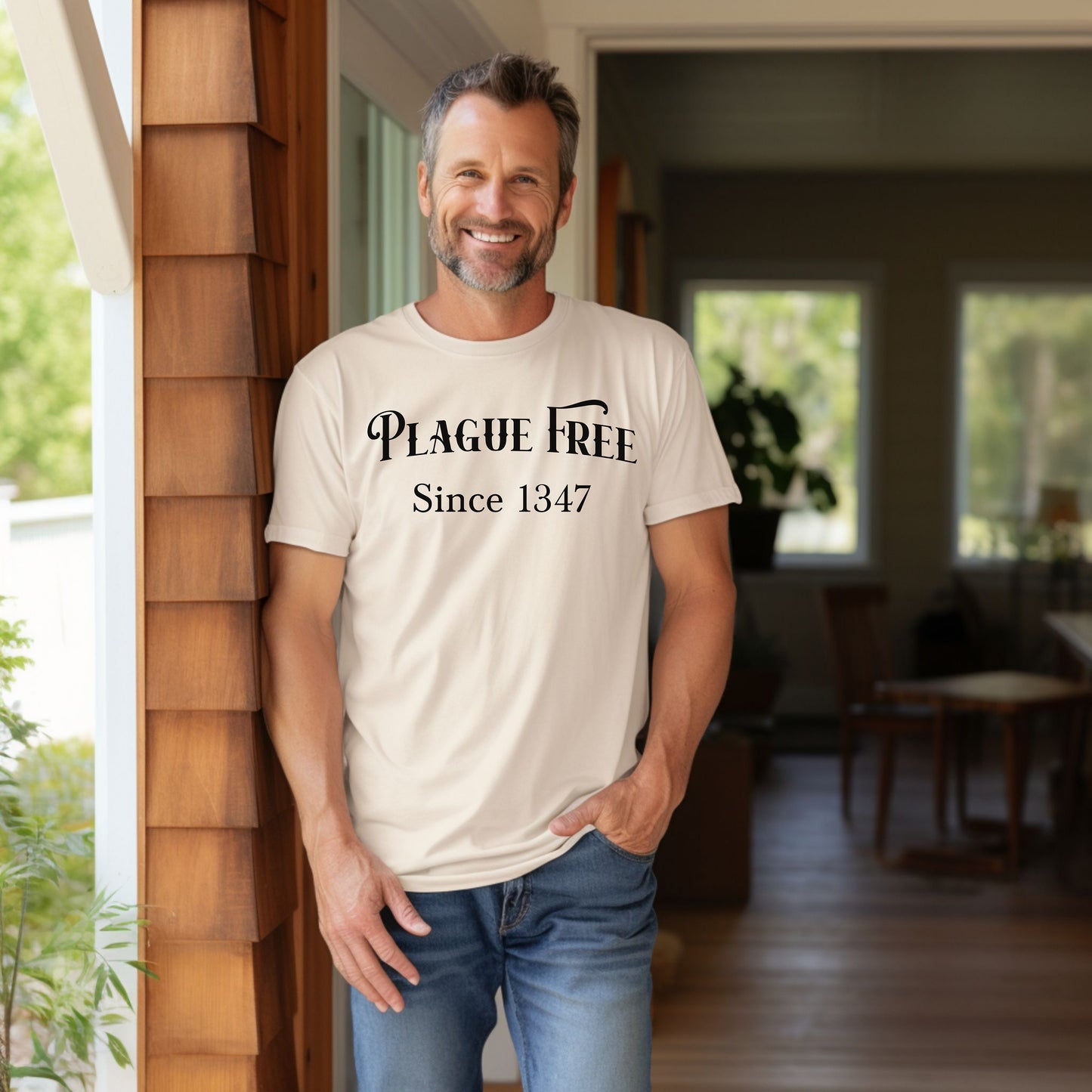 Person wearing a Ivory T-shirt with a humorous Renaissance Faire design that reads “Plague Free Since 1347” in medieval-style lettering, celebrating fair and festival fun with a nod to history. A playful shirt perfect for history buffs, medieval enthusiasts, and anyone attending a Renaissance fair or themed event.