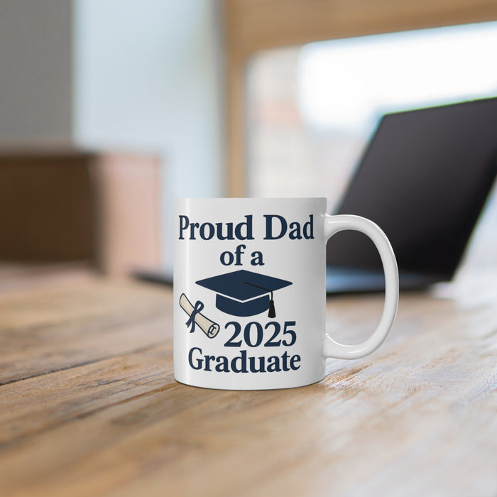 White mug with 'Proud Dad of a 2025 Graduate' text, a diploma, and a graduation cap sitting on a desk with a computer in the background.