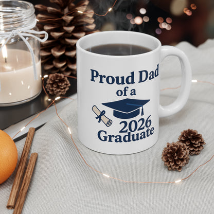 White mug with 'Proud Dad of a 2026 Graduate' text and graduation cap design, surrounded by decorative items on a table.