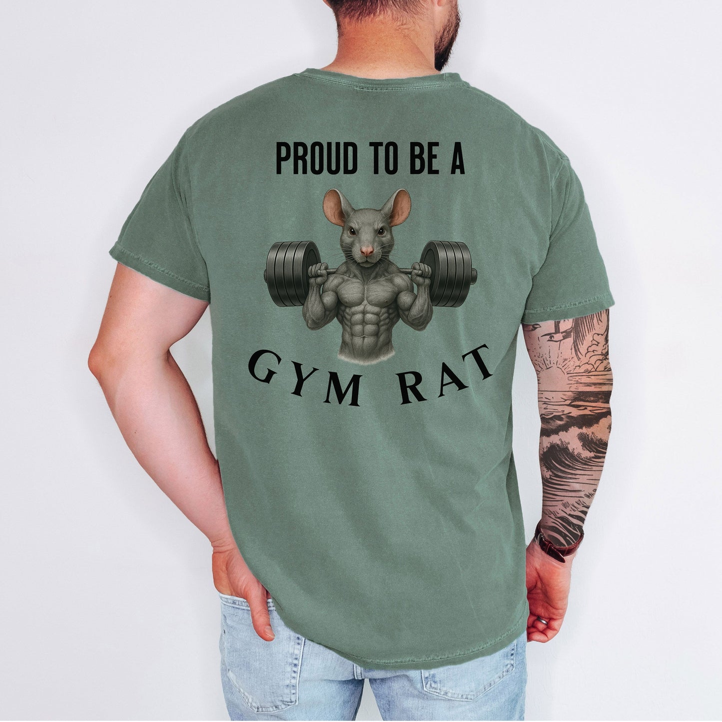 Person wearing a moss T-shirt featuring a bold back design with the phrase “Proud to Be a Gym Rat” above and below a muscular cartoon rat holding heavy dumbbells. The strong, flexing rat graphic symbolizes dedication to fitness and weightlifting, making this shirt perfect for gym lovers, bodybuilders, and strength training enthusiasts.