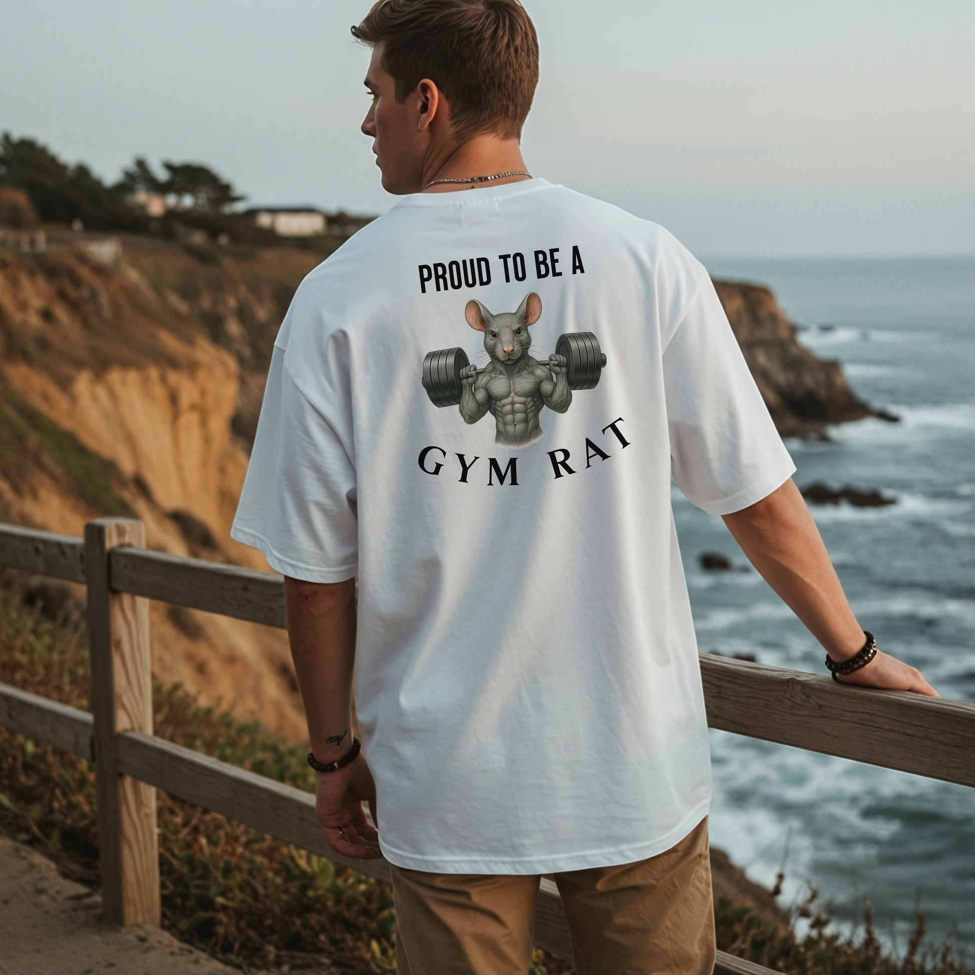 Person wearing a classic white T-shirt featuring a bold back design with the phrase “Proud to Be a Gym Rat” above and below a muscular cartoon rat holding heavy dumbbells. The strong, flexing rat graphic symbolizes dedication to fitness and weightlifting, making this shirt perfect for gym lovers, bodybuilders, and strength training enthusiasts.