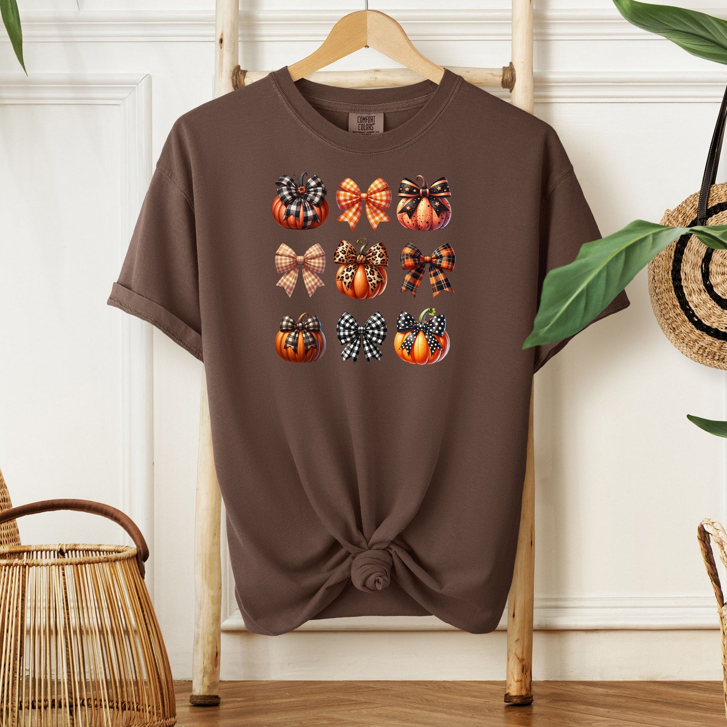 Espresso T-shirt featuring “Pumpkins and Coquette Bows” design. The artwork displays a grid of pumpkins and decorative coquette bows in plaid, gingham, and fall patterns, blending rustic autumn charm with a playful coquette aesthetic. Perfect for celebrating fall fashion and cozy seasonal vibes with a cute, stylish twist.