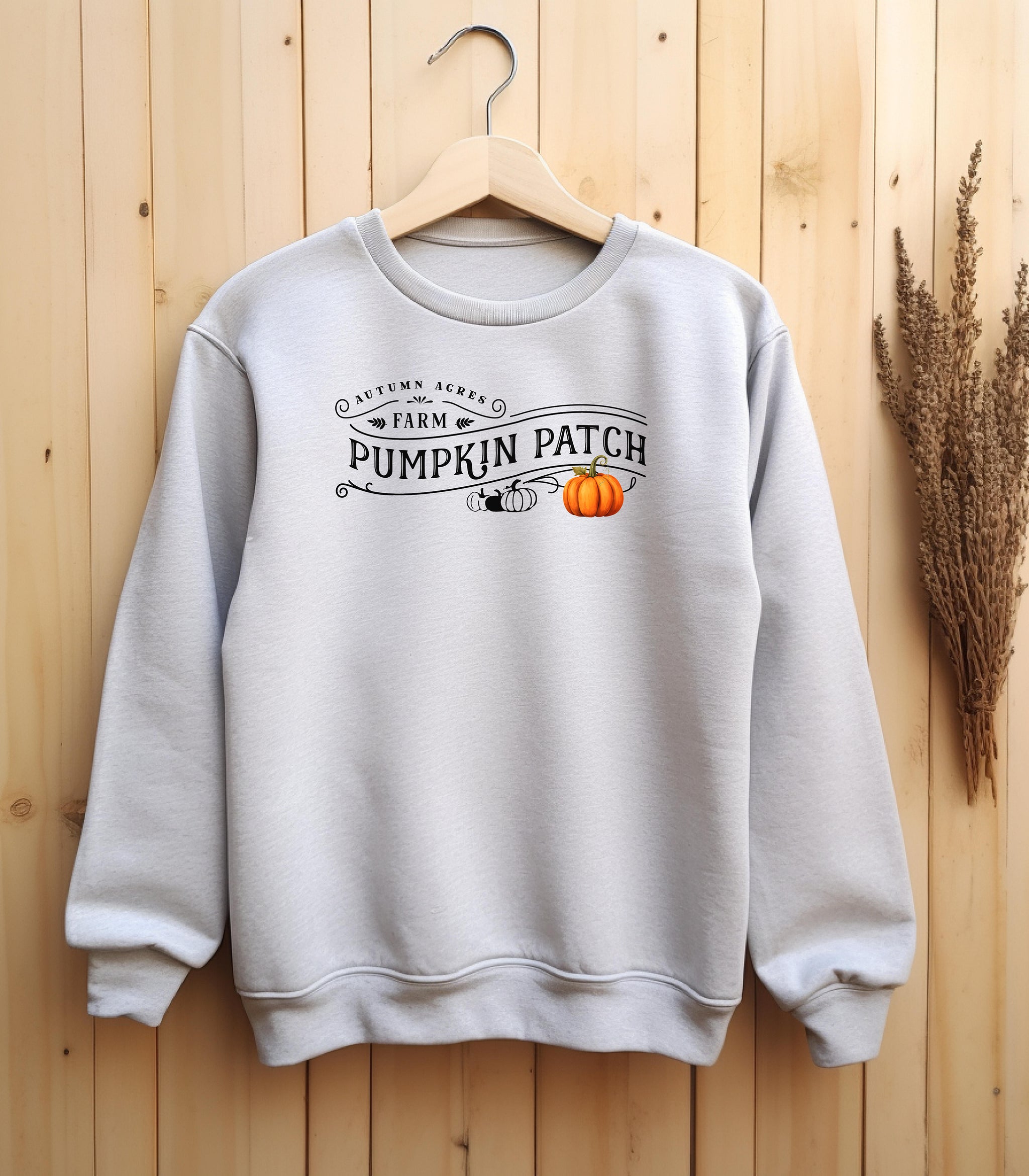 Ash Gildan sweatshirt featuring a vintage-inspired black “Autumn Acres Farm Pumpkin Patch” design with decorative swirls and white, black and orange pumpkins—on the side. A cozy, rustic fall look perfect for pumpkin picking, hayrides, and seasonal outings.