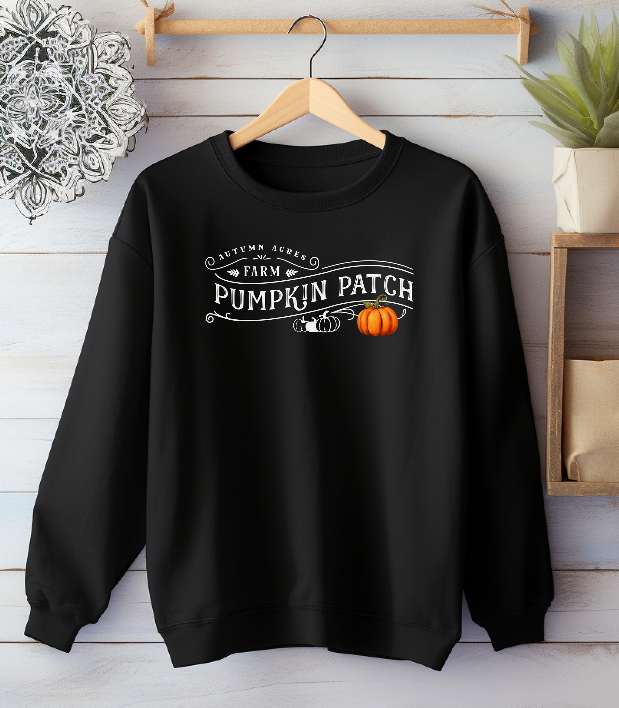 Black Gildan sweatshirt featuring a vintage-inspired white “Autumn Acres Farm Pumpkin Patch” design with decorative swirls and white, black, and orange pumpkins—on the side. A cozy, rustic fall look perfect for pumpkin picking, hayrides, and seasonal outings.