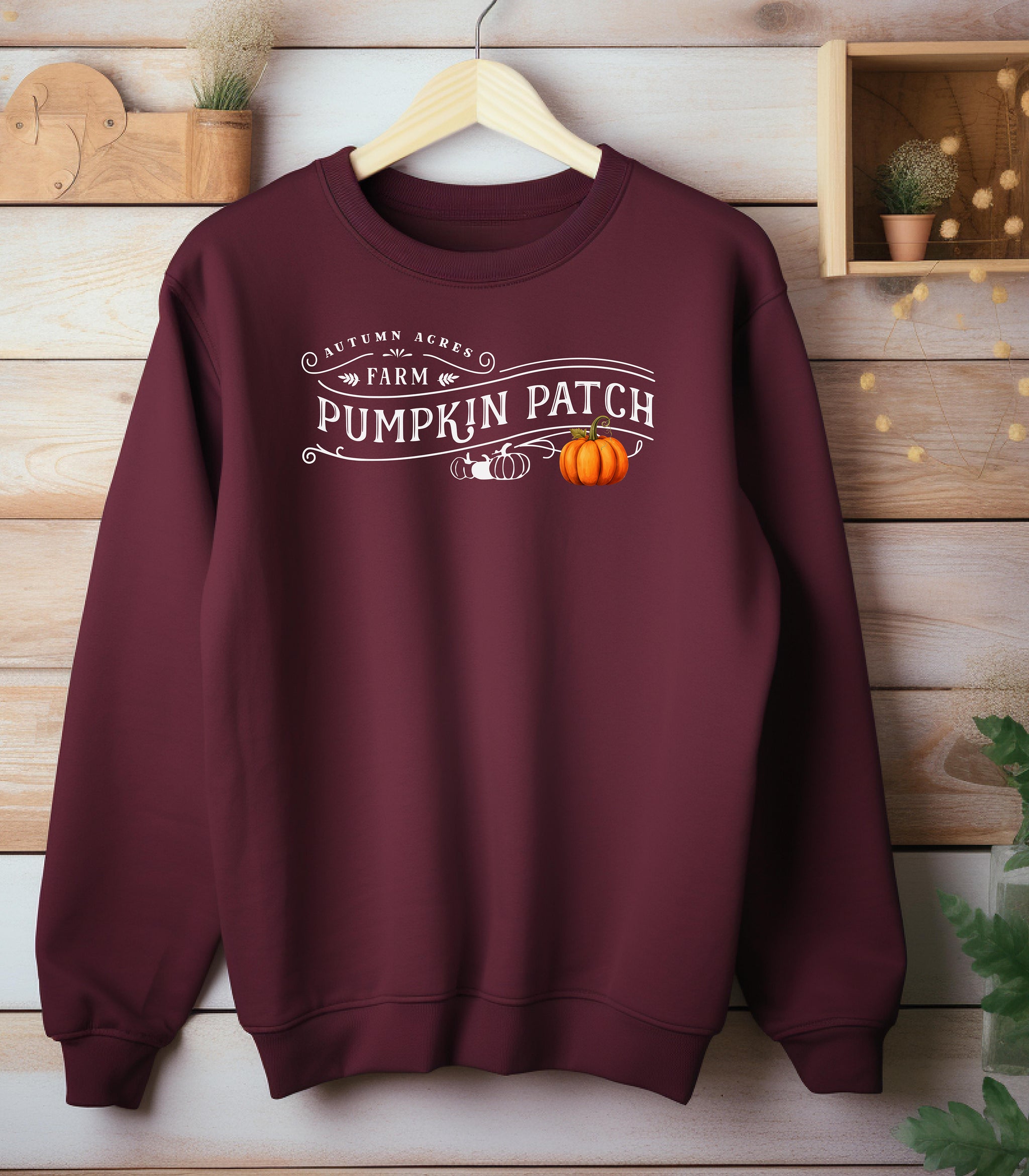 Maroon Gildan sweatshirt featuring a vintage-inspired white “Autumn Acres Farm Pumpkin Patch” design with decorative swirls and white and orange pumpkins—on the side. A cozy, rustic fall look perfect for pumpkin picking, hayrides, and seasonal outings.