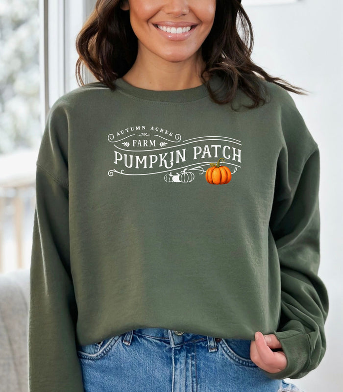 Military Green Gildan sweatshirt featuring a vintage-inspired white “Autumn Acres Farm Pumpkin Patch” design with decorative swirls and white and orange pumpkins—on the side. A cozy, rustic fall look perfect for pumpkin picking, hayrides, and seasonal outings.