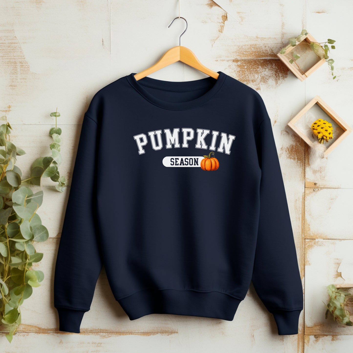 Navy blue sweatshirt with 'Pumpkin Season' text and pumpkin graphic on a wooden surface.