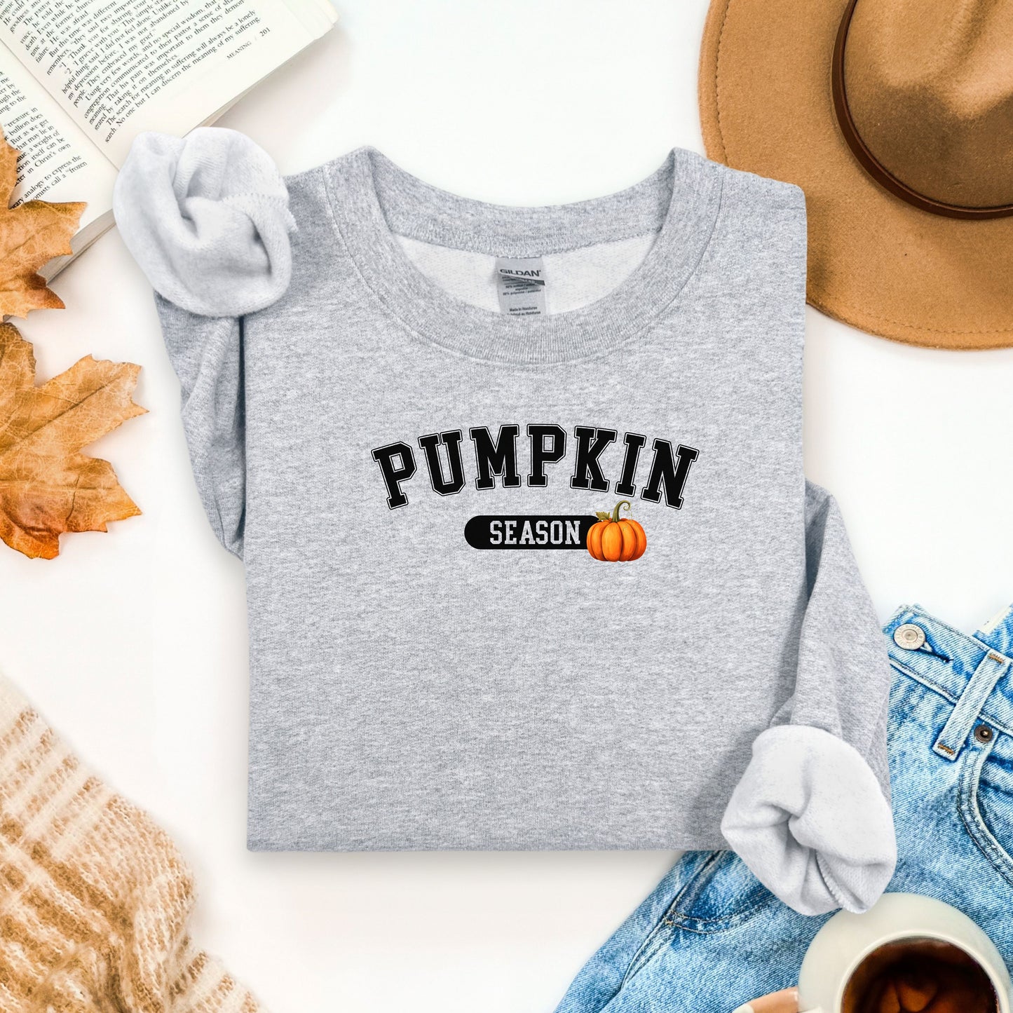 Sport Grey sweatshirt with 'Pumpkin Season' text and a pumpkin graphic on a white surface with autumn-themed items.
