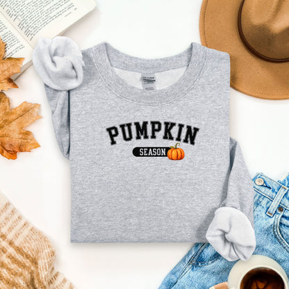 Sport Grey sweatshirt with 'Pumpkin Season' text and a pumpkin graphic on a white surface with autumn-themed items.