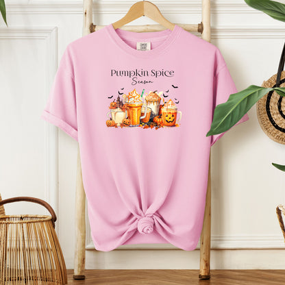 Blossom pink T-shirt featuring a “Pumpkin Spice Season” design with colorful autumn drinks topped with whipped cream, surrounded by pumpkins, jack-o’-lanterns, fall leaves, and flying bats. The cozy, festive artwork celebrates the love for pumpkin spice and autumn vibes, perfect for seasonal wear and fall enthusiasts.
