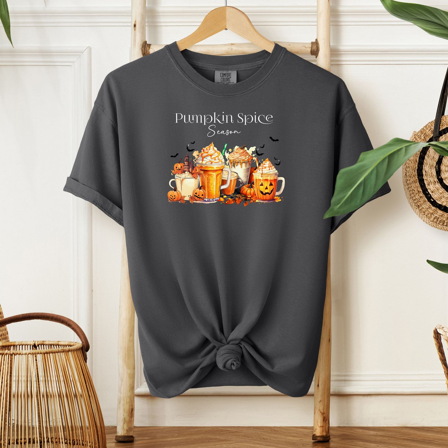 Pepper T-shirt featuring a “Pumpkin Spice Season” design with colorful autumn drinks topped with whipped cream, surrounded by pumpkins, jack-o’-lanterns, fall leaves, and flying bats. The cozy, festive artwork celebrates the love for pumpkin spice and autumn vibes, perfect for seasonal wear and fall enthusiasts.