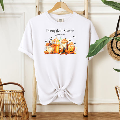 White T-shirt featuring a “Pumpkin Spice Season” design with colorful autumn drinks topped with whipped cream, surrounded by pumpkins, jack-o’-lanterns, fall leaves, and flying bats. The cozy, festive artwork celebrates the love for pumpkin spice and autumn vibes, perfect for seasonal wear and fall enthusiasts.