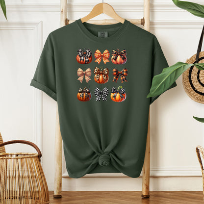 Hemp color T-shirt featuring “Pumpkins and Coquette Bows” design. The artwork displays a grid of pumpkins and decorative coquette bows in plaid, gingham, and fall patterns, blending rustic autumn charm with a playful coquette aesthetic. Perfect for celebrating fall fashion and cozy seasonal vibes with a cute, stylish twist.