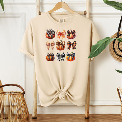 Ivory T-shirt featuring “Pumpkins and Coquette Bows” design. The artwork displays a grid of pumpkins and decorative coquette bows in plaid, gingham, and fall patterns, blending rustic autumn charm with a playful coquette aesthetic. Perfect for celebrating fall fashion and cozy seasonal vibes with a cute, stylish twist.