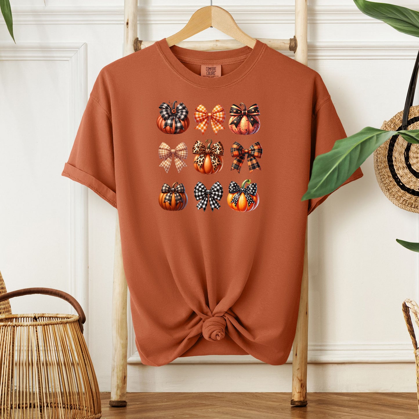 Yam T-shirt featuring “Pumpkins and Coquette Bows” design. The artwork displays a grid of pumpkins and decorative bows in plaid, gingham, and fall patterns, blending rustic autumn charm with a playful coquette aesthetic. Perfect for celebrating fall fashion and cozy seasonal vibes with a cute, stylish twist.