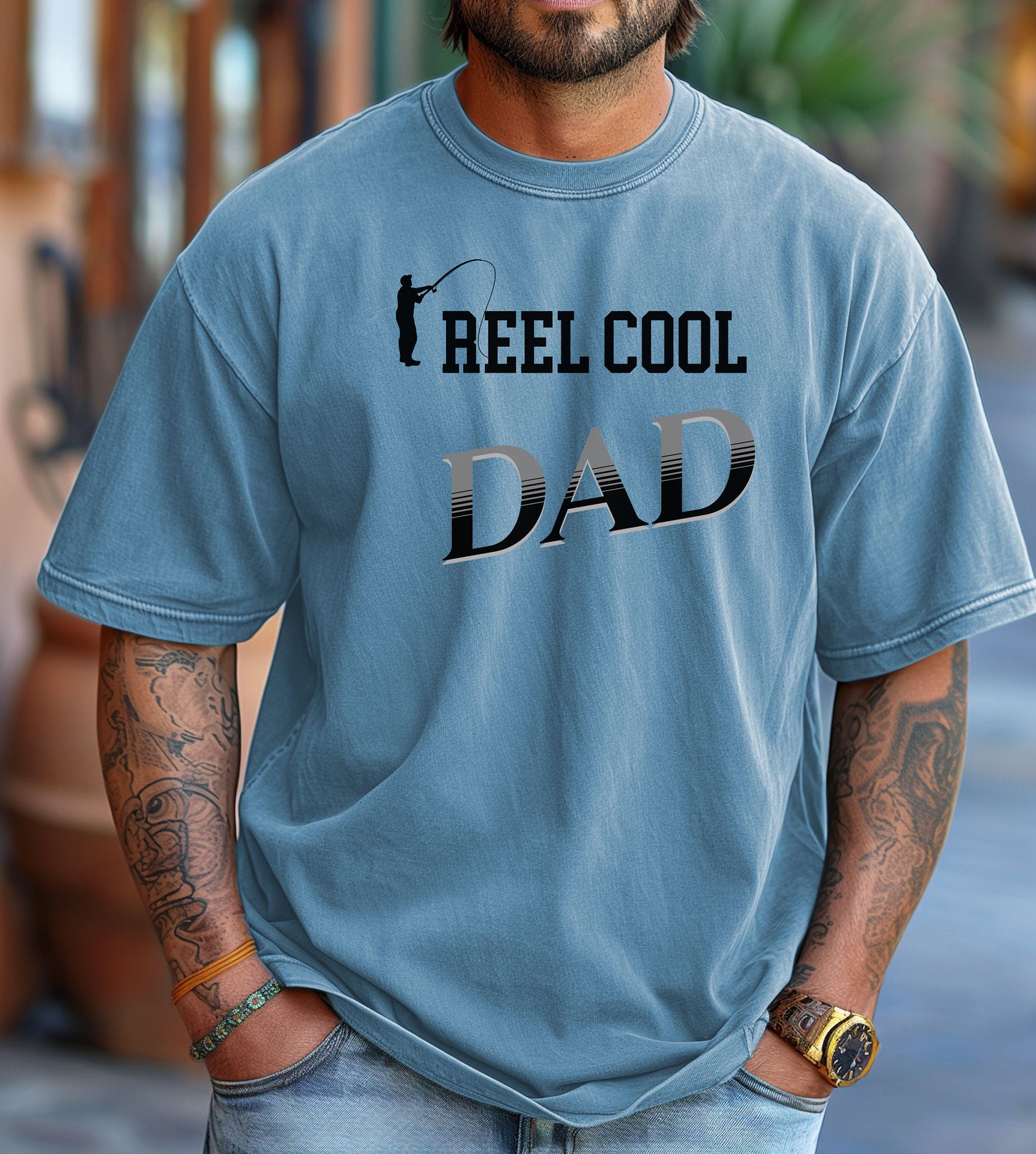 Reel Cool Dad T-shirt featuring a playful fishing-themed design with the phrase 'Reel Cool Dad' and a silhouette of a fisherman casting a line. Printed on a washed denim unisex tee, this fun graphic is perfect for dads who love fishing and spending time outdoors. Ideal for Father’s Day, birthdays, or casual wear for the proud angler dad.