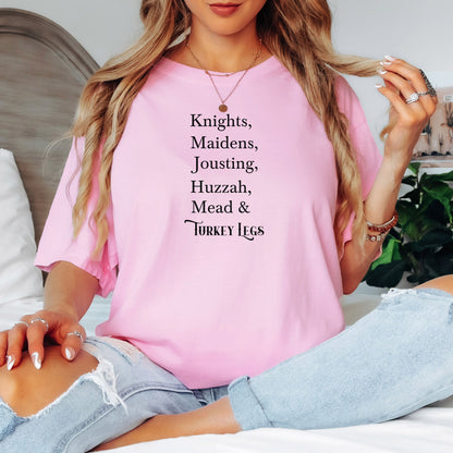 Person wearing a Blossom pink Renaissance Faire-themed T-shirt featuring a playful list-style text: “Knights, Maidens, Jousting, Huzzah, Mead & Turkey Legs.” The design uses elegant medieval-inspired fonts to celebrate classic faire experiences, perfect for fairgoers who love the festive mix of tradition, adventure, and hearty food.