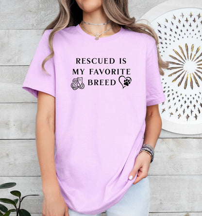 Rescued Is My Favorite Breed T-shirt featuring bold black text with small graphics of a cat, dog, and paw print heart. Printed on a lilac unisex tee, this design is perfect for animal lovers and rescue advocates. Ideal for showcasing pride in adopting pets and supporting animal rescue efforts, whether worn casually or at adoption events.