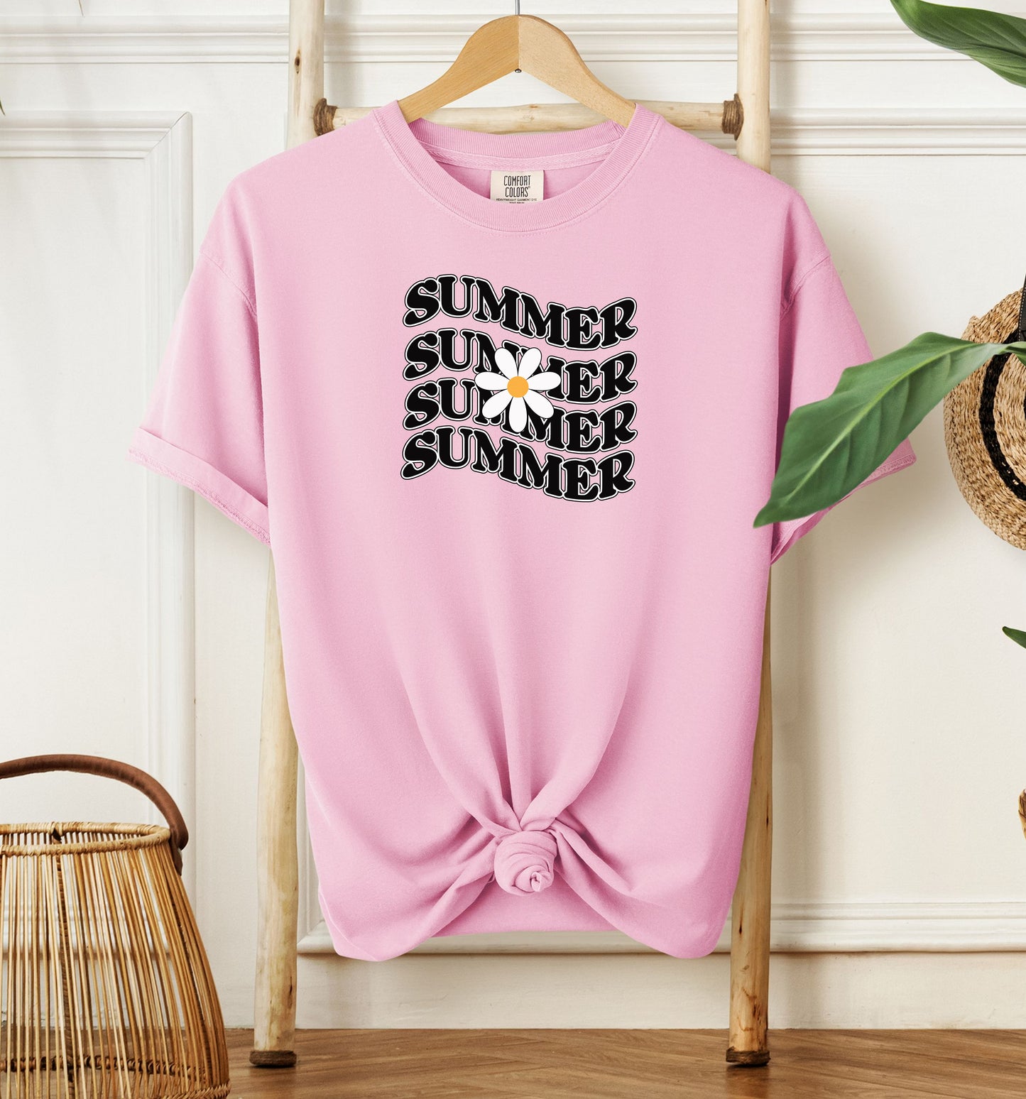 Blossom pink T-shirt featuring a retro wavy text design that repeats the word “SUMMER” four times in bold black vintage-style letters. A large white daisy with a yellow center overlaps the middle of the design, adding a cheerful floral touch. Perfect for sunny days, vacations, and casual outings, this shirt has a nostalgic, laid-back summer vibe.