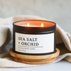 Sea Salt + Orchid soy wax blend candle in a 8 oz black matte candle tin on a wooden coaster with a neutral background