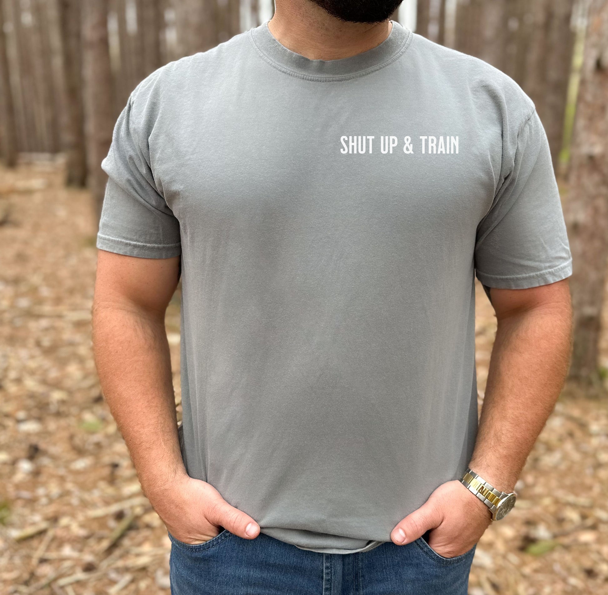 Person wearing a grey T-shirt featuring the bold motivational phrase “Shut Up & Train” in black text on the chest. The minimalist design delivers a powerful fitness message, perfect for athletes, bodybuilders, and gym-goers who embrace discipline and dedication in their workouts