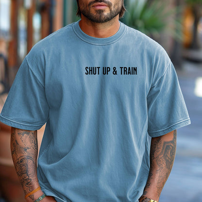 Person wearing a washed denim T-shirt featuring the bold motivational phrase “Shut Up & Train” in black text on the chest. The minimalist design delivers a powerful fitness message, perfect for athletes, bodybuilders, and gym-goers who embrace discipline and dedication in their workouts