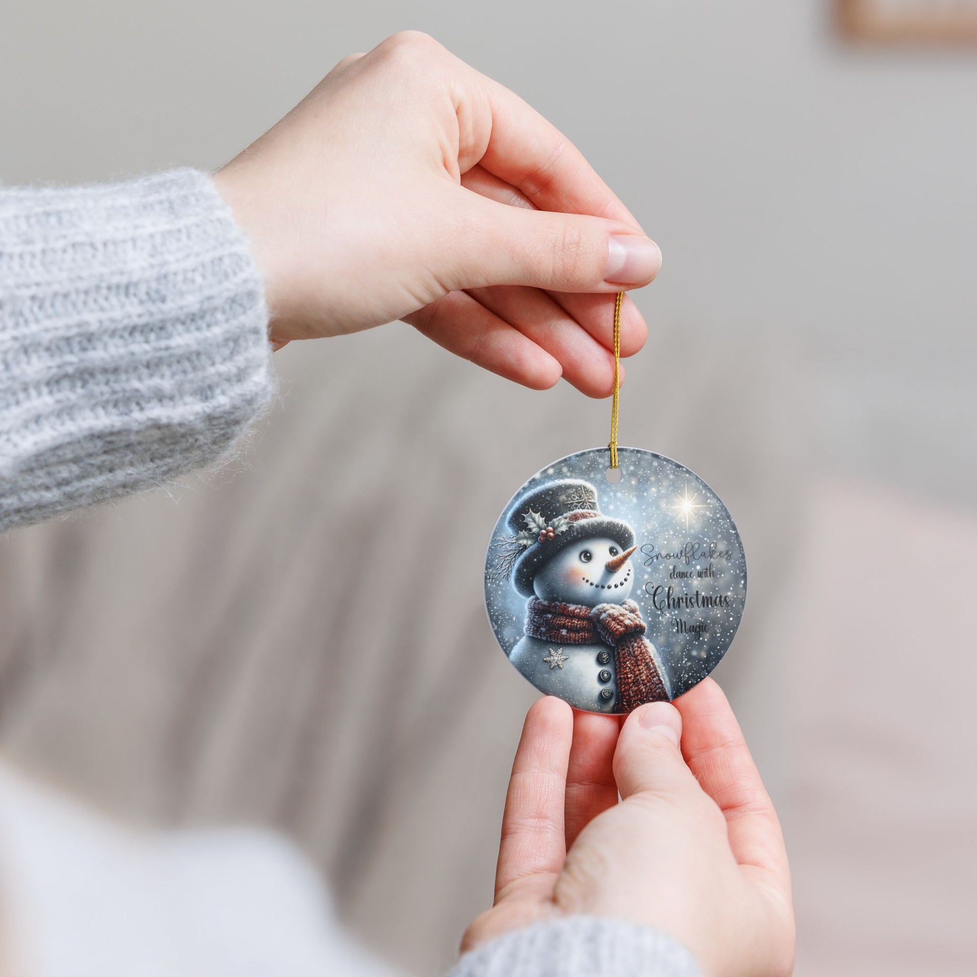 Hand holding a Christmas ornament with a snowman design against a neutral background