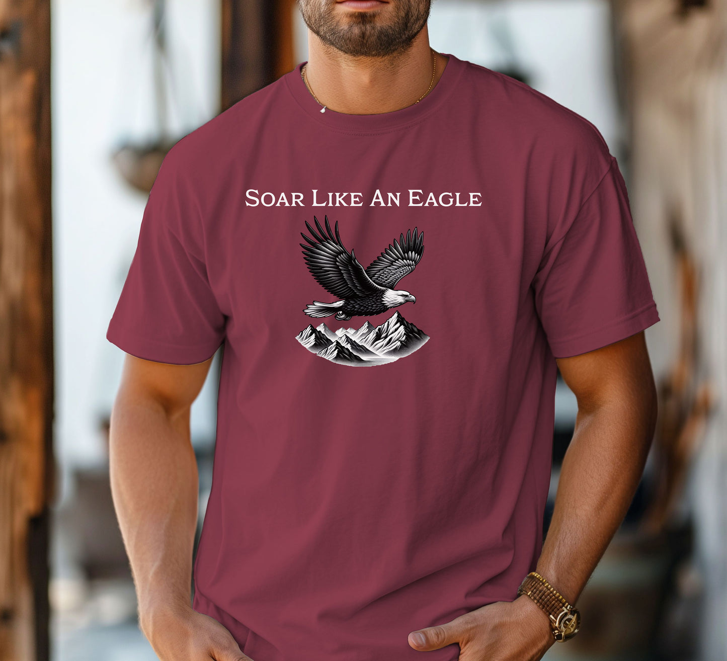 Chili T-shirt featuring a bold “Soar Like An Eagle” design with white text above a detailed black and white illustration of a soaring eagle over rugged mountain peaks. The graphic captures strength, freedom, and nature’s beauty, making it perfect for outdoor enthusiasts, adventure lovers, and patriotic spirits. Modeled in a casual, relaxed fit for everyday wear.