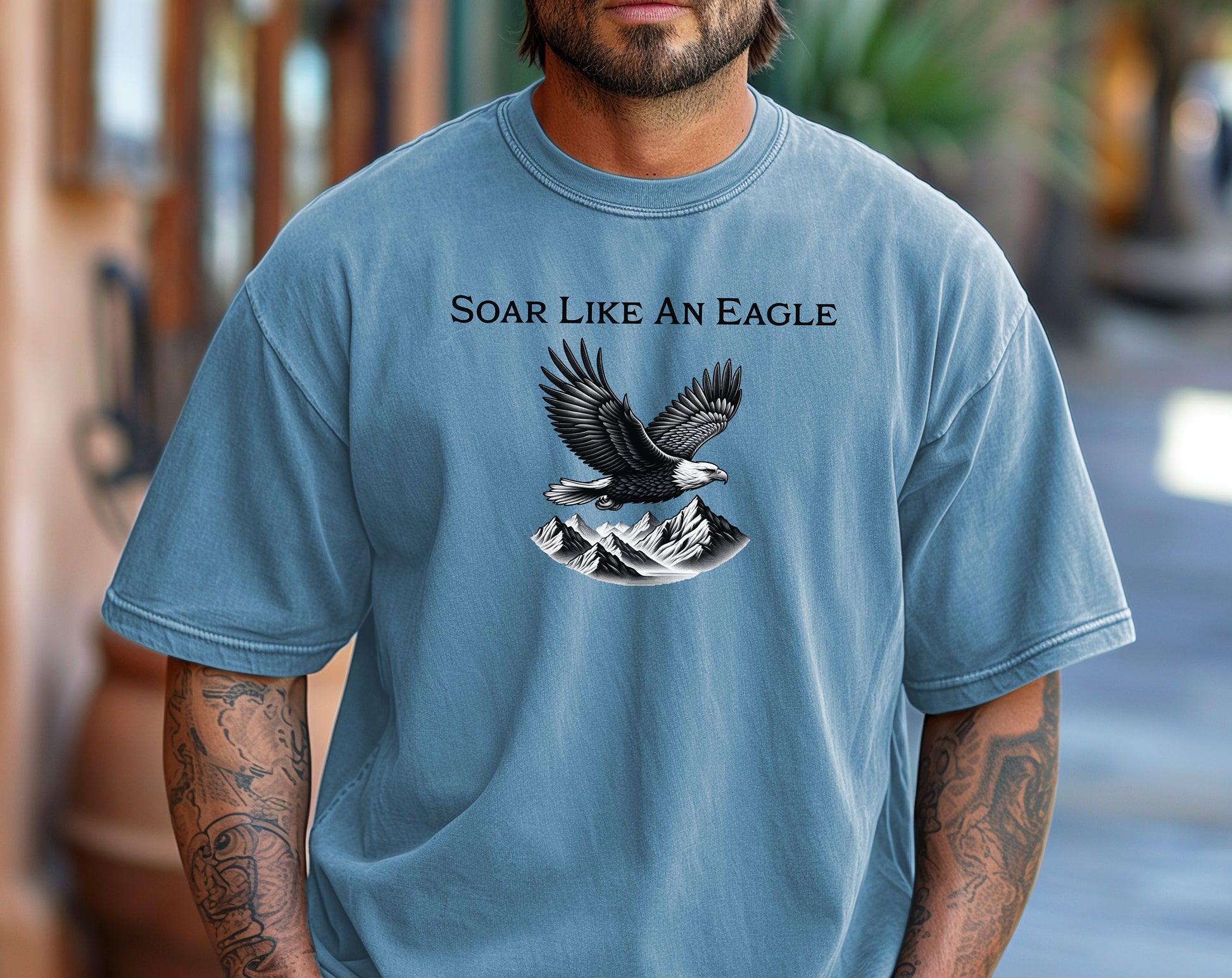 Washed Denim T-shirt featuring a bold “Soar Like An Eagle” design with white text above a detailed black and white illustration of a soaring eagle over rugged mountain peaks. The graphic captures strength, freedom, and nature’s beauty, making it perfect for outdoor enthusiasts, adventure lovers, and patriotic spirits. Modeled in a casual, relaxed fit for everyday wear.