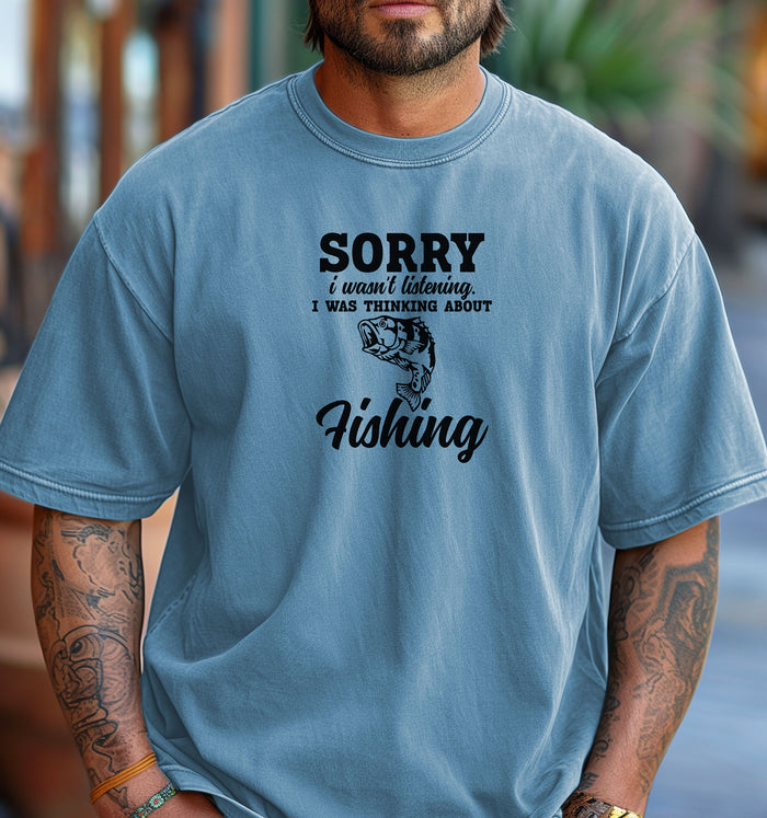 SORRY I wasn’t listening. I was thinking about Fishing' T-shirt featuring bold and script fonts with a detailed fish illustration. Printed on a washed denim unisex tee, this humorous design is perfect for fishing enthusiasts who’d rather be on the water than anywhere else. Ideal for casual wear, fishing trips, or as a fun gift for anglers and dads who love the sport.