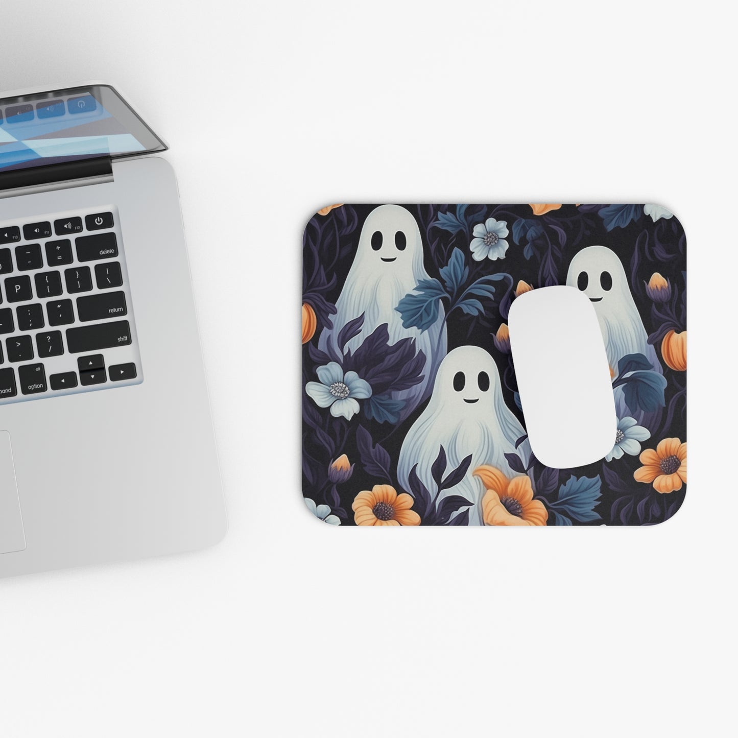 Mouse pad with cute ghost design next to a laptop on a white surface