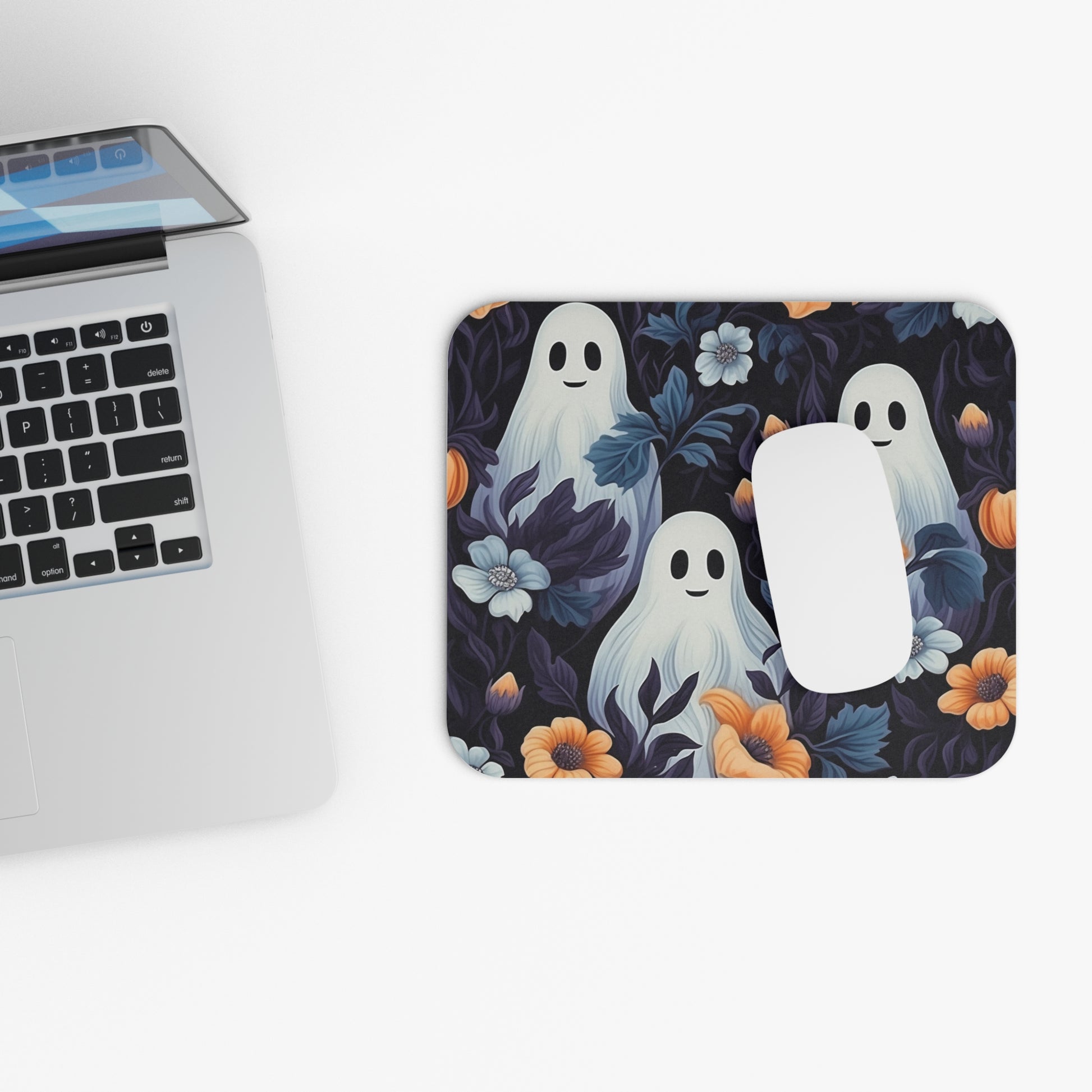 Mouse pad with cute ghost design next to a laptop on a white surface
