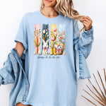 Spring Is In The Air T-shirt in soft baby blue featuring a charming Sprint and Easter design with a white bunny wearing a pink coquette bow, colorful tulips, carrots, pastel eggs, rain boots, and a floral basket. The background includes vertical pastel paint strokes in pink, yellow, blue, and navy, adding a cheerful seasonal touch perfect for spring and Easter celebrations.