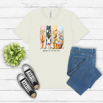 Spring Is In The Air T-shirt in citron featuring a charming Sprint and Easter design with a white bunny wearing a pink coquette bow, colorful tulips, carrots, pastel eggs, rain boots, and a floral basket. The background includes vertical pastel paint strokes in pink, yellow, blue, and navy, adding a cheerful seasonal touch perfect for spring and Easter celebrations.