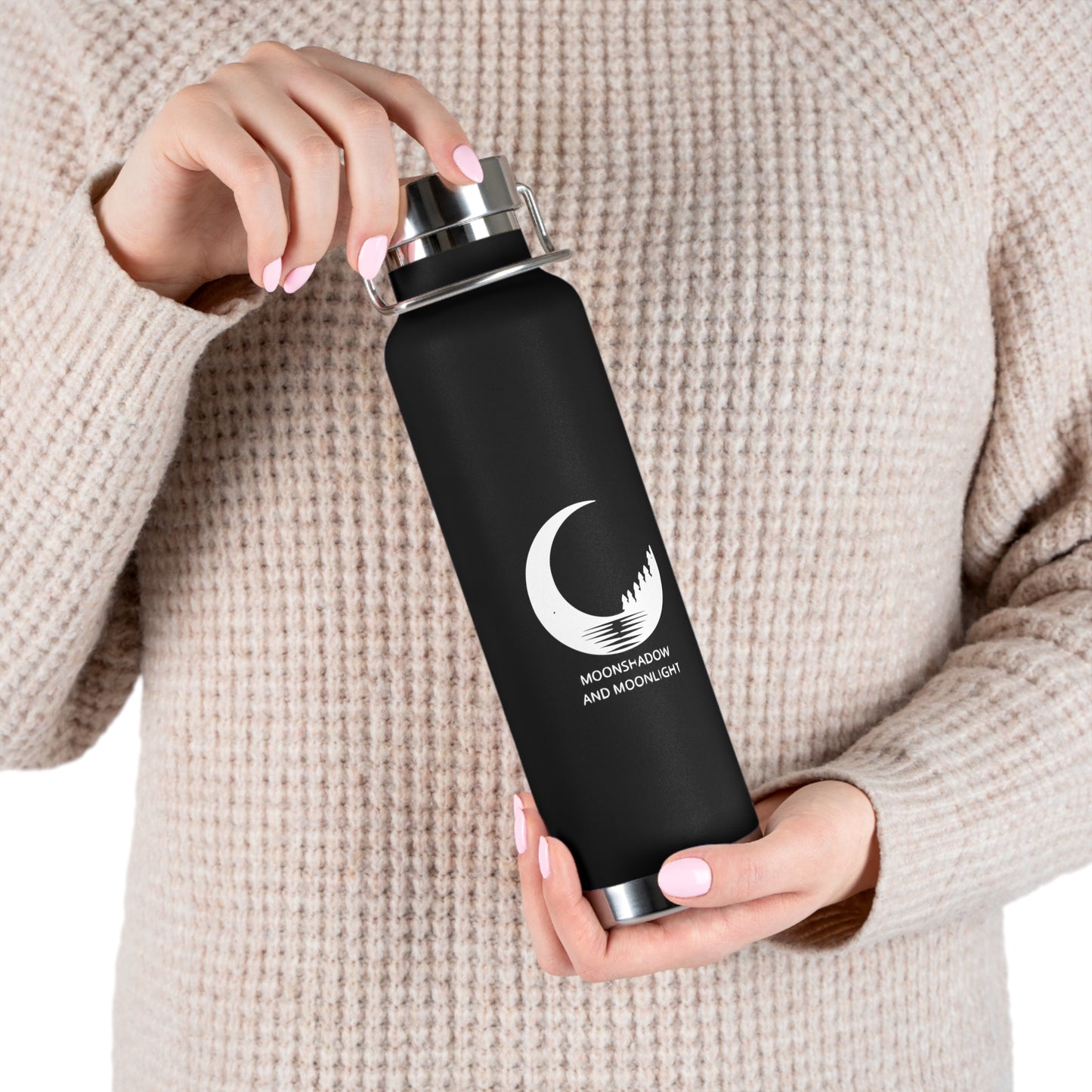 Person holding a black water bottle with a logo and text, wearing a beige sweater.