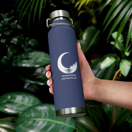Navy blue water bottle with a logo held by a hand against a leafy green background