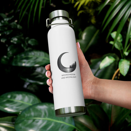 White water bottle with a moon design held by a hand against a green leafy background