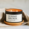 Sunday Brunch soy wax blend candle in a 8 oz black matte candle tin on a wooden coaster with a beige cloth background