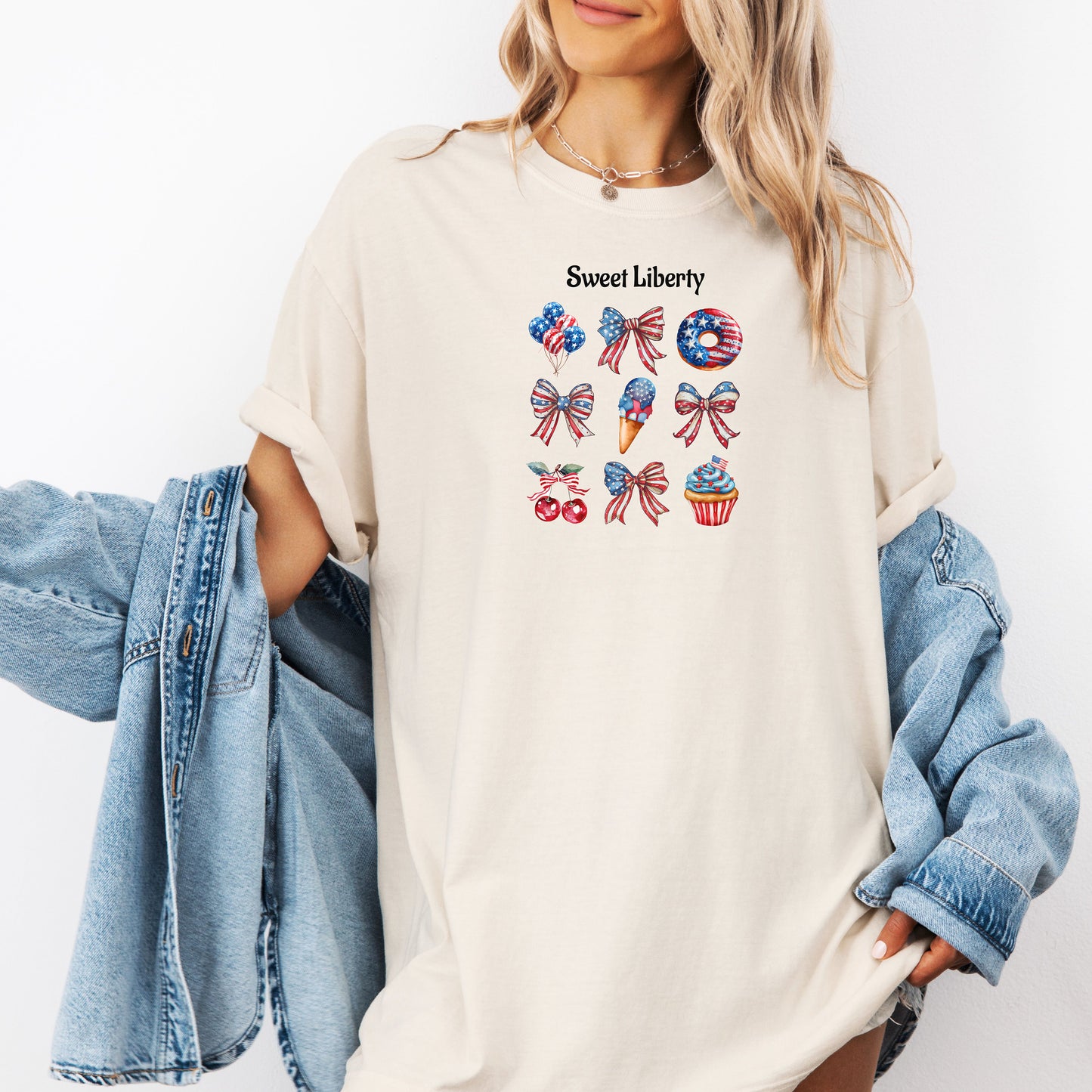 Ivory t-shirt featuring a festive 'Sweet Liberty' design with patriotic icons including bows, cherries, a donut, ice cream cone, and cupcake decorated in red, white, and blue stars and stripes. Fun, colorful 4th of July and summer celebration shirt perfect for parties, barbecues, and casual wear.