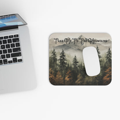 Mouse pad with mountain design and 'Take Me To The Mountains' text next to a laptop on a white background