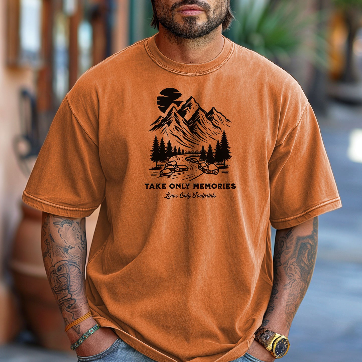 Yam unisex T-shirt featuring a black minimalist outdoor design of mountains, pine trees, and a winding river under a crescent moon. Below the scene, the text reads “Take Only Memories, Leave Only Footprints” in elegant script and bold font. Modeled with a casual denim jacket for a relaxed, nature-inspired style.