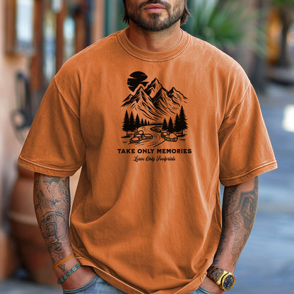 Yam unisex T-shirt featuring a black minimalist outdoor design of mountains, pine trees, and a winding river under a crescent moon. Below the scene, the text reads “Take Only Memories, Leave Only Footprints” in elegant script and bold font. Modeled with a casual denim jacket for a relaxed, nature-inspired style.