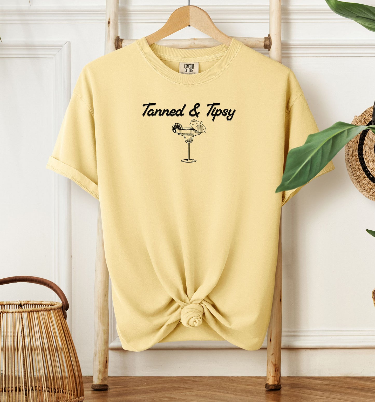 Banana T-shirt featuring the fun phrase “Tanned & Tipsy” with a simple line art illustration of a margarita glass garnished with a lime wedge and a tiny cocktail umbrella. Perfect for summer beach parties, vacations, or casual outings, this relaxed and playful shirt embodies sunny vibes and carefree fun.