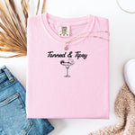 Blossom pink T-shirt featuring the fun phrase “Tanned & Tipsy” with a simple line art illustration of a margarita glass garnished with a lime wedge and a tiny cocktail umbrella. Perfect for summer beach parties, vacations, or casual outings, this relaxed and playful shirt embodies sunny vibes and carefree fun.