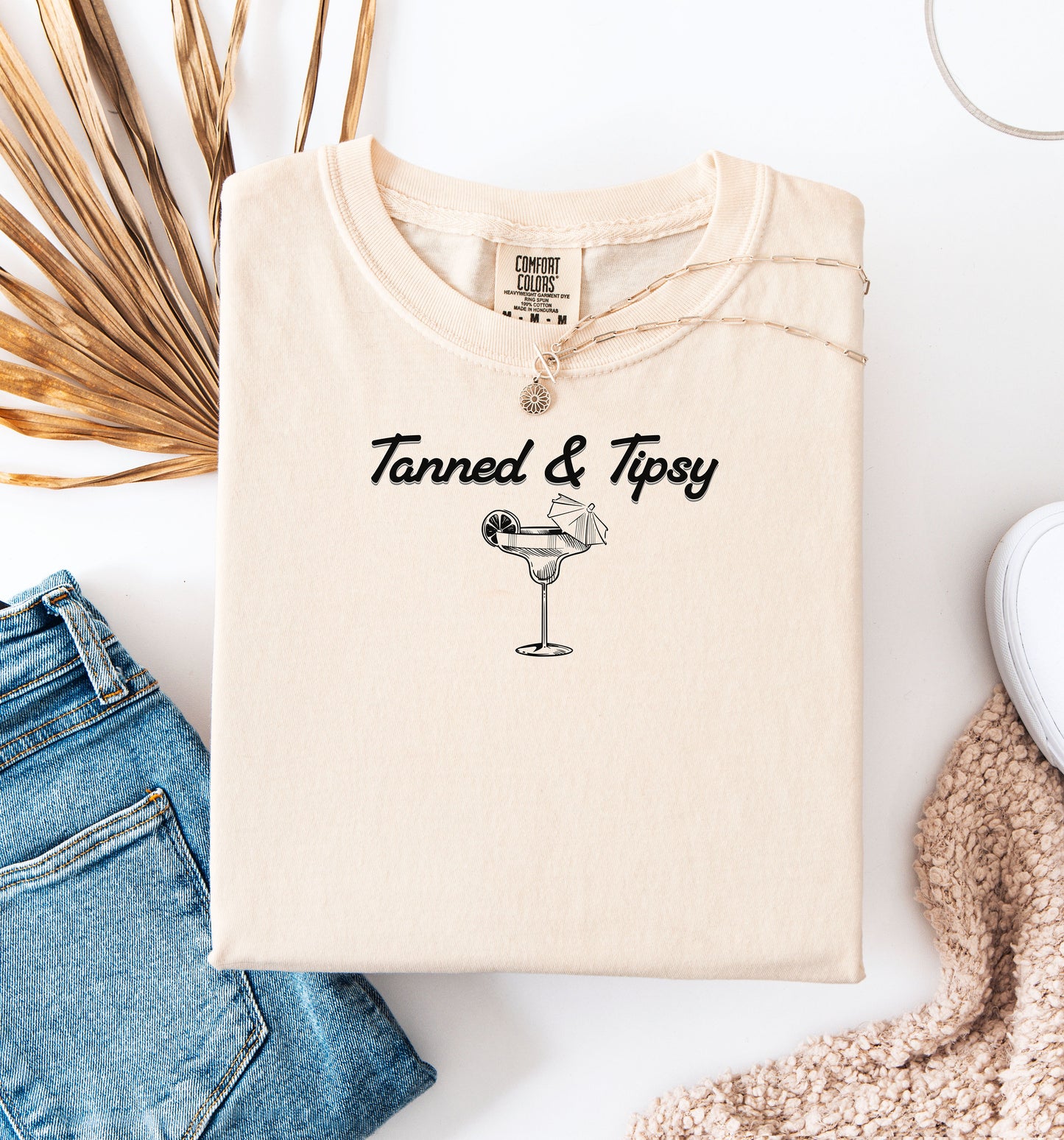 Ivory T-shirt featuring the fun phrase “Tanned & Tipsy” with a simple line art illustration of a margarita glass garnished with a lime wedge and a tiny cocktail umbrella. Perfect for summer beach parties, vacations, or casual outings, this relaxed and playful shirt embodies sunny vibes and carefree fun.