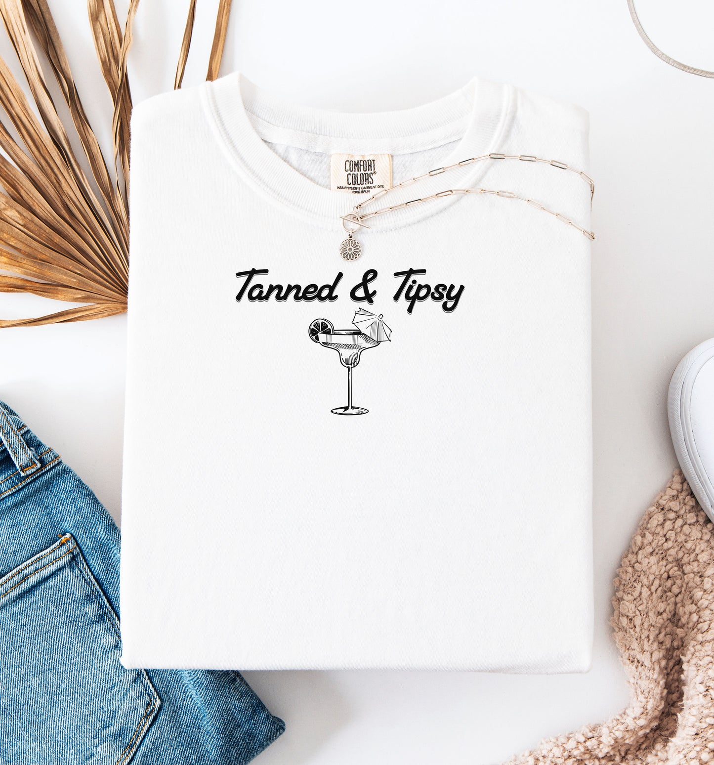 Tanned Tipsy T-shirt featuring the fun phrase “Tanned & Tipsy” with a simple line art illustration of a margarita glass garnished with a lime wedge and a tiny cocktail umbrella. Perfect for summer beach parties, vacations, or casual outings, this relaxed and playful shirt embodies sunny vibes and carefree fun.