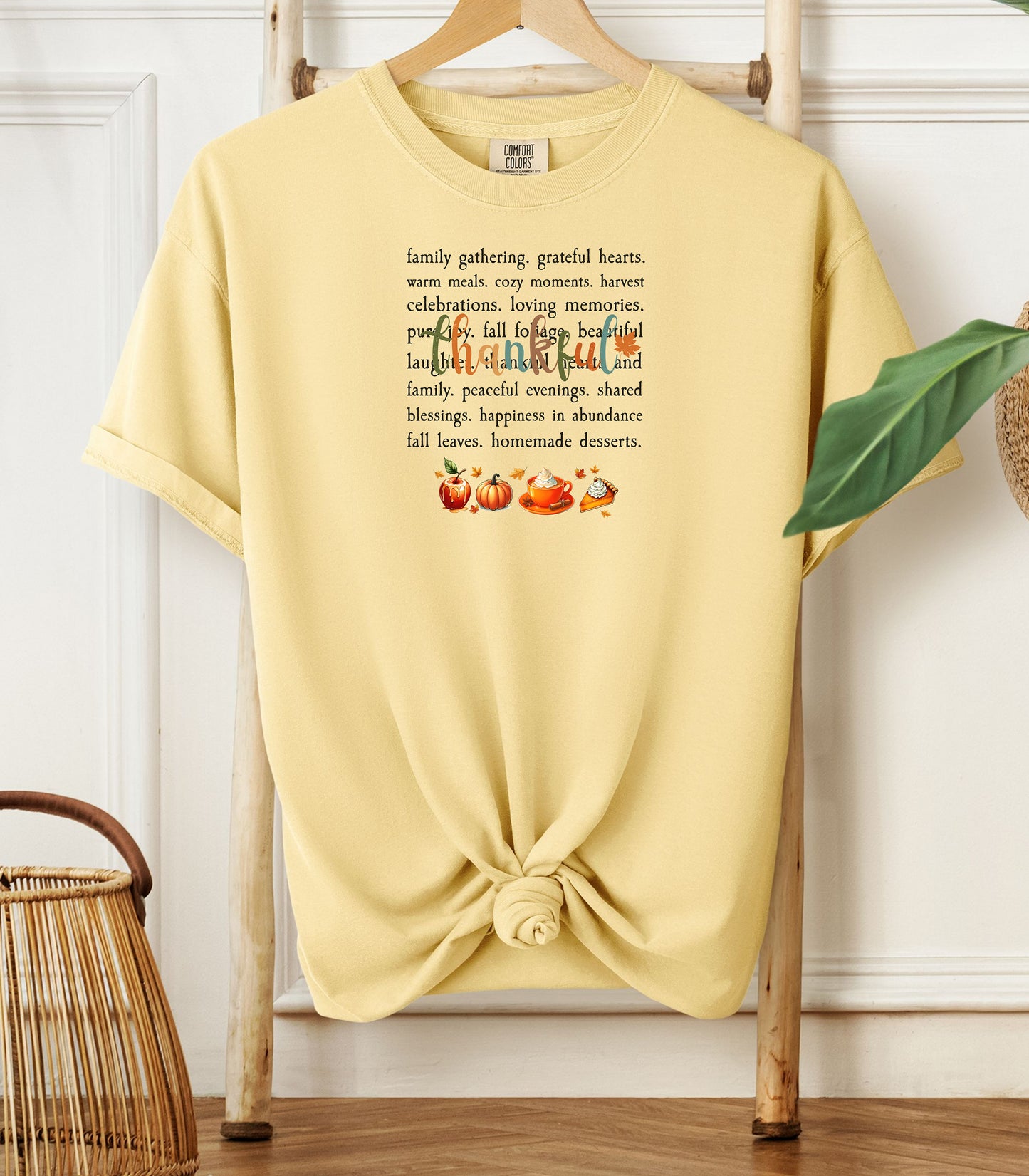 A banana soft yellow T-shirt with a festive “Thankful” harvest-themed design featuring fall words like family gathering, grateful hearts, cozy moments, and homemade desserts, with autumn illustrations of an apple, pumpkin, pie, and fall leaves. A warm and cheerful tee perfect for Thanksgiving, family gatherings, or celebrating the fall season.