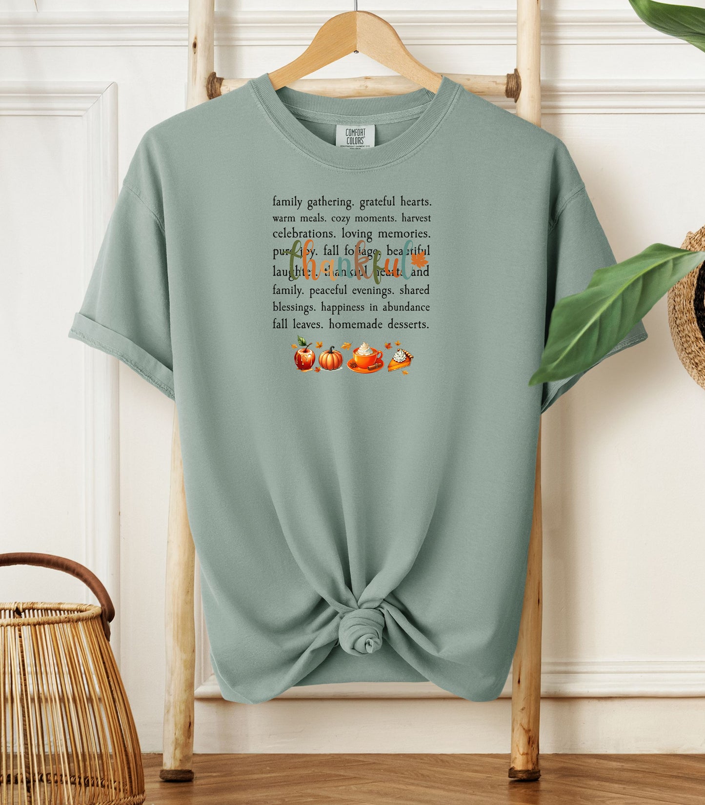 A Bay light green T-shirt with a festive “Thankful” harvest-themed design featuring fall words like family gathering, grateful hearts, cozy moments, and homemade desserts, with autumn illustrations of an apple, pumpkin, pie, and fall leaves. A warm and cheerful tee perfect for Thanksgiving, family gatherings, or celebrating the fall season.